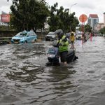 Warga dan pengendara melintasi jalan yang terendam banjir akibat hujan deras di wilayah perkotaan, ilustrasi banjir di Kabupaten Tangerang.