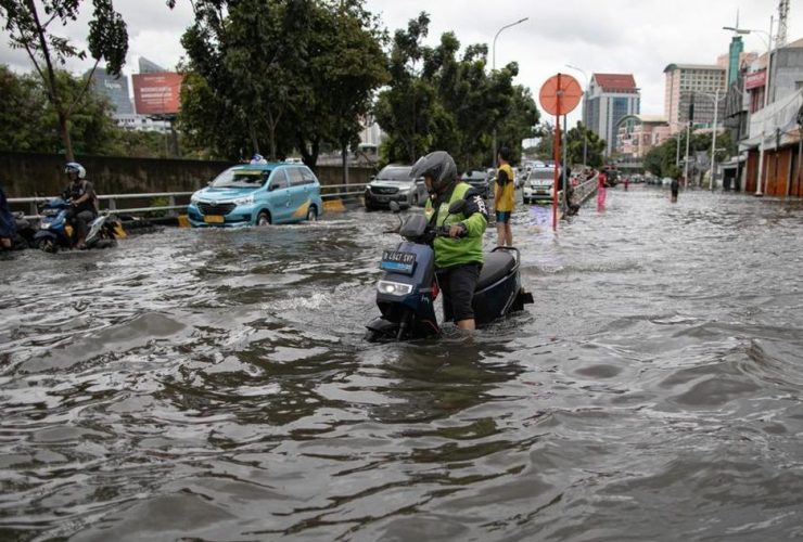 Warga dan pengendara melintasi jalan yang terendam banjir akibat hujan deras di wilayah perkotaan, ilustrasi banjir di Kabupaten Tangerang.