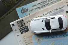 Ilustrasi dokumen kendaraan bermotor seperti STNK dan BPKB dengan miniatur mobil di atasnya terkait kebijakan baru pajak kendaraan