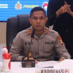 Kapolres Tangerang Selatan mengenakan seragam Polri saat memberikan keterangan pers di ruang konferensi, dengan papan nama “Kapolres” di meja dan petugas bahasa isyarat di belakangnya.